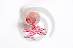 Pink pills spill out from bottle isolated on white background.