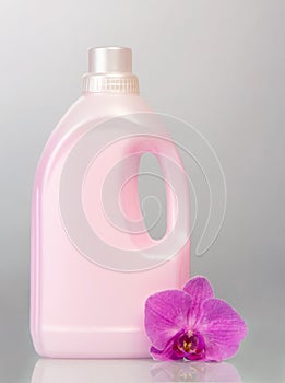 Pink plastic bottle with liquid detergent, orchid flower on gray.