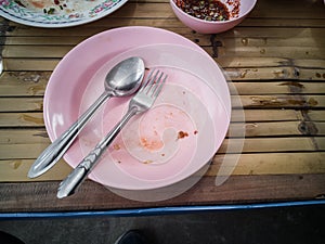 Pink plastic dish, spoon and fork steel are table wooden with copy space