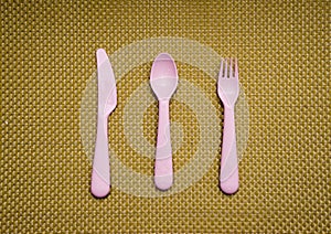 Pink, plastic spoon, fork, knife lie on brown background
