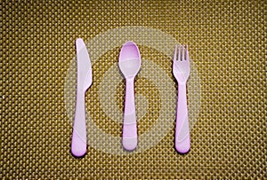 Pink, plastic spoon, fork, knife lie on brown background