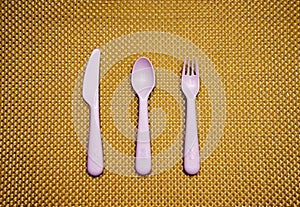 Pink, plastic spoon, fork, knife lie on brown background