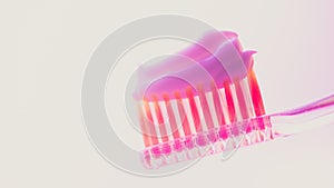 Pink plastic toothbrush with a thick layer of white toothpaste on an isolated background