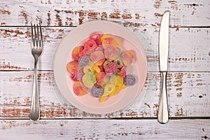 Pink plate with gummy candies on white wooden background.