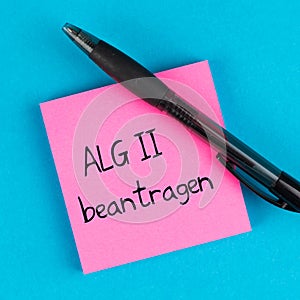 Pink post with pen on blue background and german text ALG 2 beantragen, in english apply for unemployment benefits