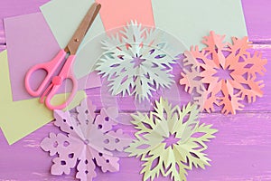 Pink, purple, blue, green paper cut snowflakes, stationery craft supplies on wood background. Merry Christmas paper snowflakes