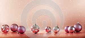 Pink and purple Christmas tree balls on pinkish orange coral background with falling snow