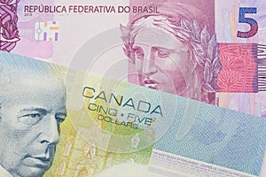 A pink and purple five real bank note from Brazil paired with a blue five dollar bill from Canada.