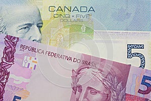 A pink and purple five real bank note from Brazil paired with a blue five dollar bill from Canada.