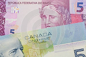 A pink and purple five real bank note from Brazil paired with a blue five dollar bill from Canada.