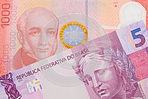 A pink and purple five real bank note from Brazil paired with a colorful red one thousand colones bank note from Costa Rica.