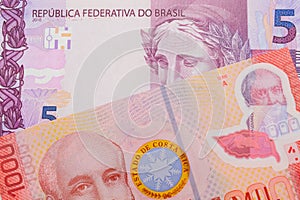 A pink and purple five real bank note from Brazil paired with a colorful red one thousand colones bank note from Costa Rica.
