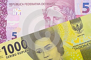 A pink and purple five real bank note from Brazil paired with a green one thousand bank note from Indonesia.