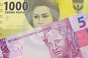 A pink and purple five real bank note from Brazil paired with a green one thousand bank note from Indonesia.