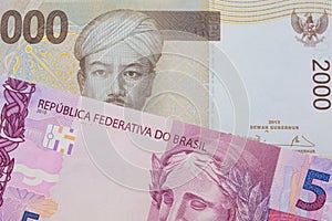 A pink and purple five real bank note from Brazil paired with a grey two thousand Indonesian rupiah bank note.