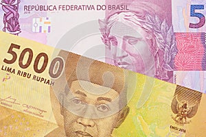 A pink and purple five real bank note from Brazil paired with a orange five thousand Indonesian rupiah note.