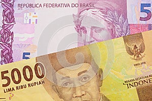 A pink and purple five real bank note from Brazil paired with a orange five thousand Indonesian rupiah note.