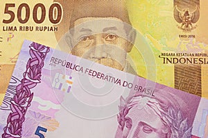 A pink and purple five real bank note from Brazil paired with a orange five thousand Indonesian rupiah note.