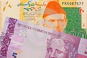 A pink and purple five real bank note from Brazil paired with a orange and green 20 rupee note from Pakistan.