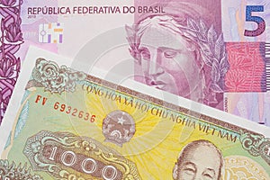 A pink and purple five real bank note from Brazil paired with a yellow one thousand dong bill from Vietnam.