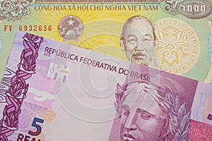 A pink and purple five real bank note from Brazil paired with a yellow one thousand dong bill from Vietnam.