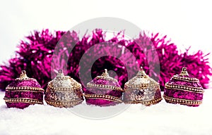 Pink and purple and gold Christmas balls in snow with tinsel, christmas background