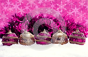 Pink and purple and gold Christmas balls in snow with tinsel and snowflakes, christmas background