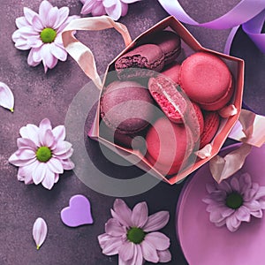 Pink and purple macaroon close-up in a gift paper bag on a purple background decorated with flowers. Top view, selective focus.