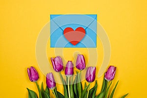 Pink, purple tulips and blue coral envelope with one red heart on it on yellow background