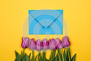 Pink, purple tulips and blue coral envelope with one red heart on it on yellow background