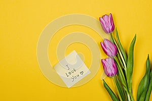 Pink, purple tulips and a sticky note saying I love you on yellow background