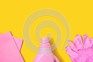 Pink rag, plastic bottle and rubber gloves on yellow background. Cleaning concept