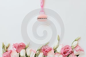 Pink razor with blades on a light gray background with rose flowers at the bottom of the frame