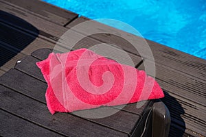 Pink, red towel on a brown sunbed by the pool in summer at the resort