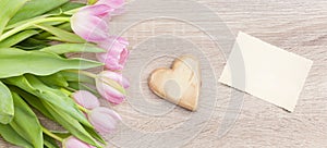 Pink red tulips on a light wooden table with wooden heart and postcard