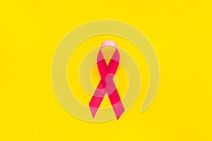 Pink ribbon as symbol of breast cancer awareness on yellow background top view space for text