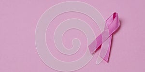 Pink ribbon breast cancer awareness symbol on pink background. Panoramic image with copy space.