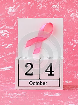 Pink ribbon of breast cancer awareness on a white wooden perpetual calendar with date 24 october. International breast cancer