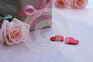 Pink ribbon gift box, orange-pink roses and red satin hearts on vintage wooden table for Valentine& x27;s concept