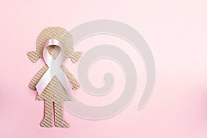 Pink ribbon with girl cardboard doll on pink background for Breast Cancer Awareness symbol.