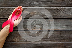 Pink ribbon in hands as symbol of breast cancer awareness on dark wooden background top view space for text