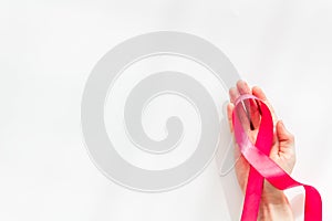 Pink ribbon in hands as symbol of breast cancer awareness on white background top view space for text