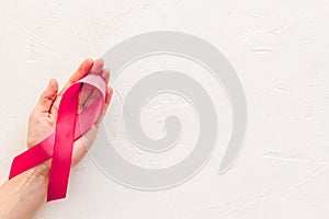 Pink ribbon in hands as symbol of breast cancer awareness on white background top view space for text