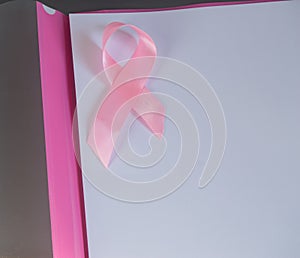 Pink ribbon on a piece of paper to raise awareness breast cancer, copy space