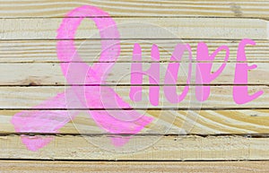 A pink ribbon shape is hand-painted on natural, raw wood planking with copy space on the right side.