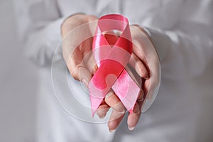 Pink ribbon in woman hands for breast cancer awareness, symbolic bow color raising awareness on people living with breast tumor