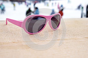 Pink-rimmed sunglasses on wooden slope in aprÃ¨s ski bar or cafe, with ski slope in background, copy space. Concept of winter