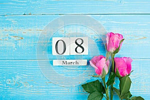 Pink rose flower and 8th March calendar on blue wood table background with copy space for text. Love, Equal and International