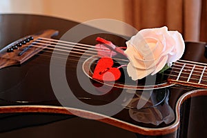 Pink rose flower and red hearts on the strings of a dark guitar.