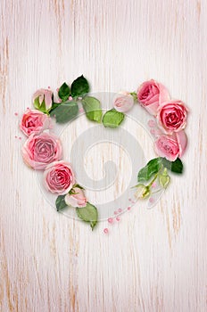 Pink rose flowers, buds and glitter confetti in a heart shape arrangement on white wooden background